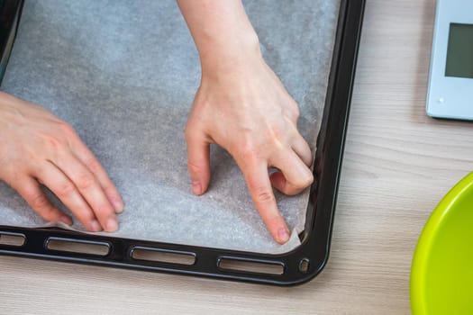 Hands hold baking paper on a tray. Preparing homemade cake.