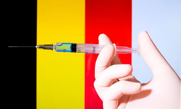 Hand in surgery glove holding syringe with covid vaccine. Belgian flag in the background