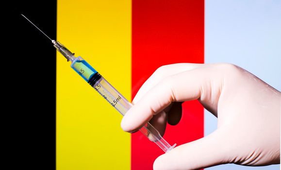 Hand in surgery glove holding syringe with covid vaccine. Belgian flag in the background