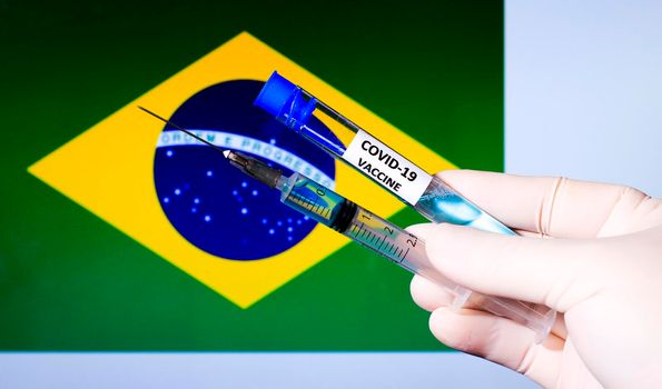 Hand in surgery glove holding syringe with covid vaccine. Brazilian flag in the background