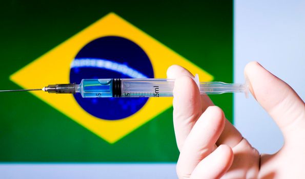 Hand in surgery glove holding syringe with covid vaccine. Brazilian flag in the background