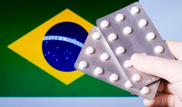 Hand in surgical glove holding pill blisters. Brazilian flag in the background