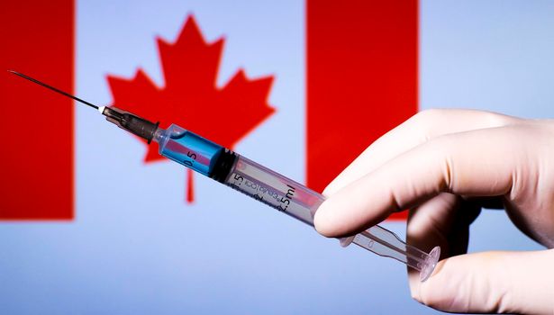 Hand in surgery glove holding syringe with covid vaccine. Canadian flag in the background