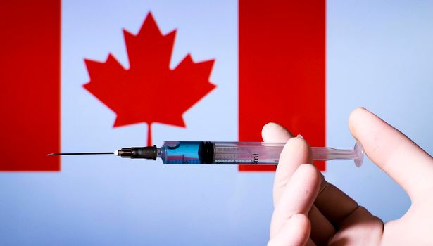 Hand in surgery glove holding syringe with covid vaccine. Canadian flag in the background
