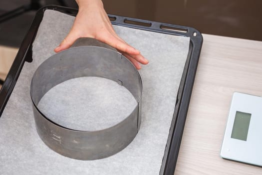 Hand holds iron cake form on baking paper on a tray. Preparing homemade cake.