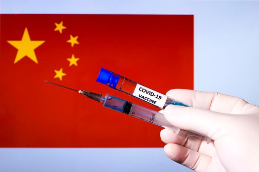 Hand in surgery glove holding syringe with covid vaccine. China flag in the background