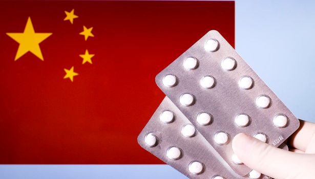 Hand in surgical glove holding pill blisters. China flag in the background