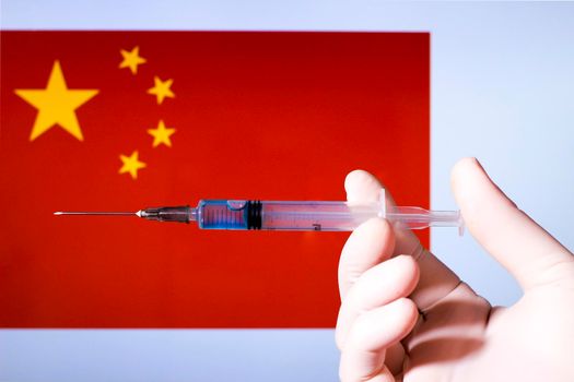 Hand in surgery glove holding syringe with covid vaccine. China flag in the background
