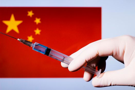 Hand in surgery glove holding syringe with covid vaccine. China flag in the background
