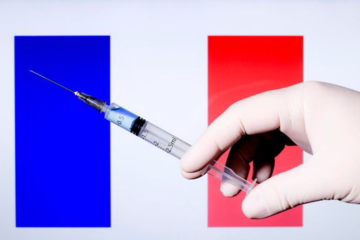 Hand in surgery glove holding syringe with covid vaccine. French flag in the background