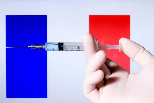 Hand in surgery glove holding syringe with covid vaccine. French flag in the background