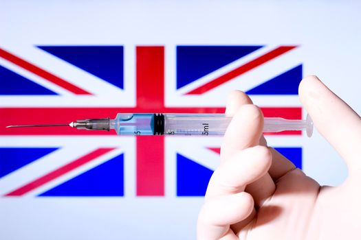 Hand in surgery glove holding syringe with covid vaccine. British flag in the background