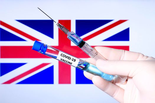 Hand in surgery glove holding syringe with covid vaccine. British flag in the background