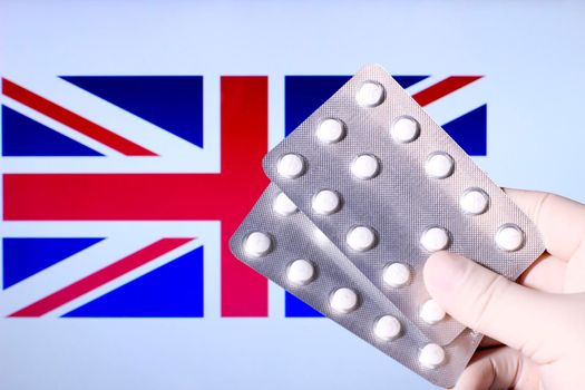 Hand in surgical glove holding pill blisters. Great Britain flag in the background