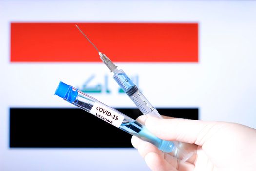 Hand in surgery glove holding syringe with covid vaccine. Iraqi flag in the background