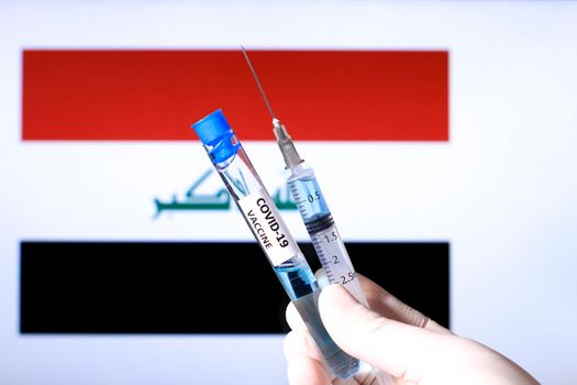 Hand in surgery glove holding syringe with covid vaccine. Iraqi flag in the background