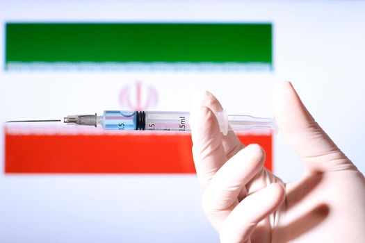 Hand in surgery glove holding syringe with covid vaccine. Iranian flag in the background