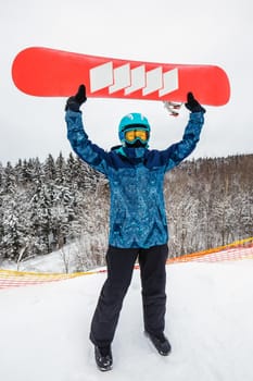 Female in a blue suit standing with a snowboard on a large snow slope. Snowboarder holds the snowboard over his head. Skiing holidays. Logoisk, Belarus