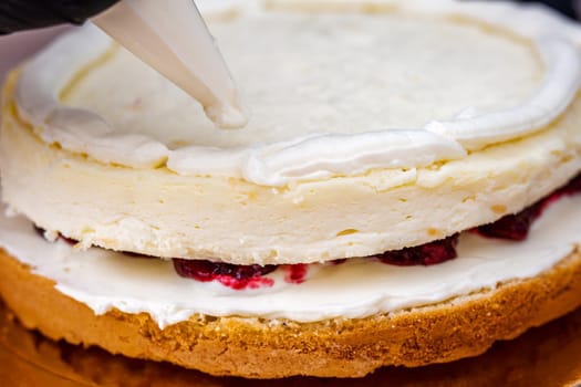 Female hand in black glove squeezes out cream on a cheesecake with coconut.