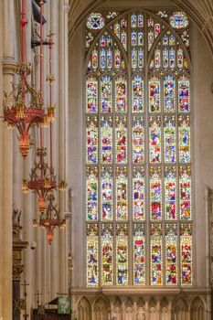 Wide-shot of the lamps, altar and a big stained glass window at Bath Abbey on a sunny day
