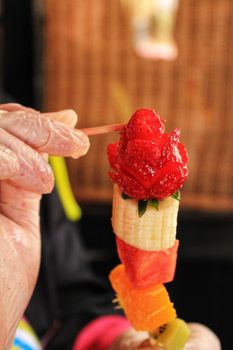 Cook hands with gloves preparing colorful fruit skewers