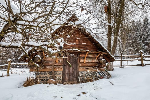 Decorated wooden house with textured wall and bycicle covered with a heavy snow in the village in Belarus.