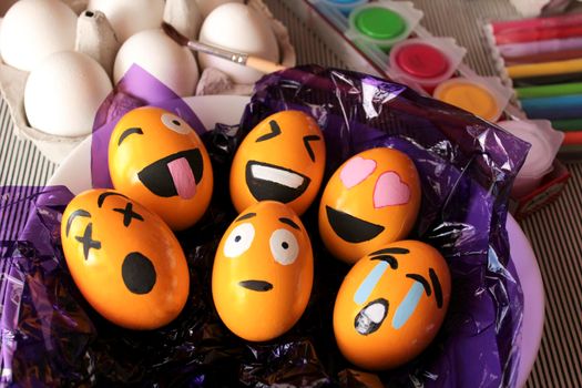 Alicante, Spain- March 18, 2021: Emoticons Easter Eggs on purple cellophane paper. More white eggs, brush and paints in the background.