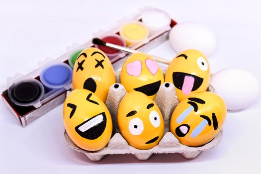 Alicante, Spain- March 18, 2021: Emoticons Easter Eggs in egg-cup , paints and brush with white background