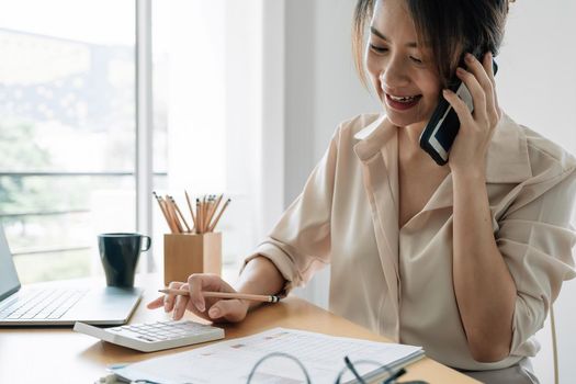 Young accountant hand holding smartphone to call marketing consultants and using laptop computer to analyze sales growth in the global workplace market. accounting concept.