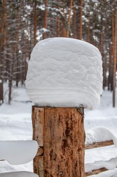 Large snow caps on the stumps of the fence in winter. A wooden fence protects the territory of the house.