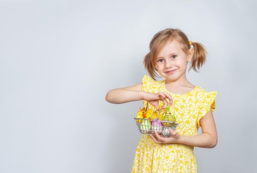 Portrait of a little cute Caucasian smiling girl with a shopping basket filled with Easter decorations. Easter background with place to insert text.