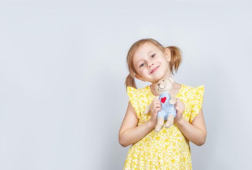 Little Caucasian girl with teddy bear looking at the camera, advertisement posing against studio wall. Advertising concept