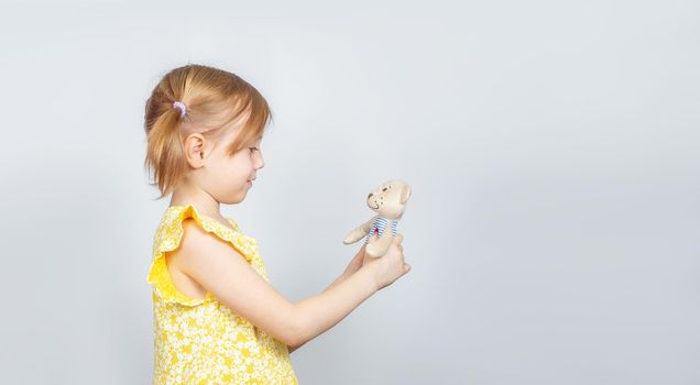 Little Caucasian girl with teddy bear standing sideways to the camera, advertisement posing against studio wall. Advertising concept