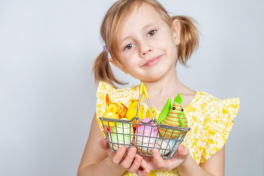 Portrait of a little cute Caucasian smiling girl with a shopping basket filled with Easter decorations. Easter background with place to insert text.