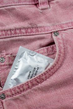 Close-up of a pocket of pink jeans from which a condom sticks out, safe sex concept