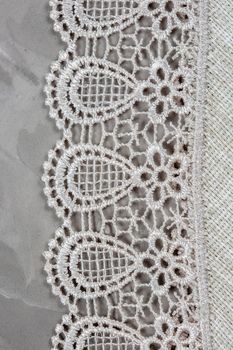Close-up of a piece of factory lace on gray concrete background.