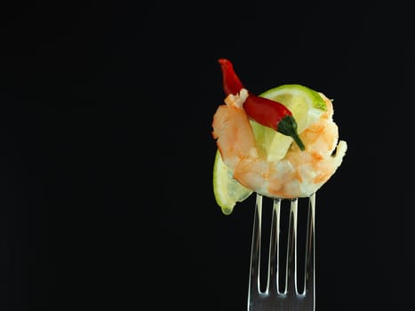 Boiled shrimp on a fork with a piece of lime, isolated on a black background. High quality photo