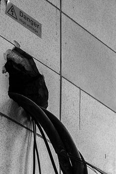 Close-up of a tiled wall with a hole and cables appearing through it and a danger sign on top