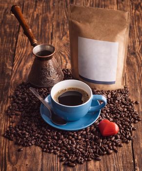 blue cup of coffee, beans, turkish coffee pot, and craft paper pouch bag on wooden background