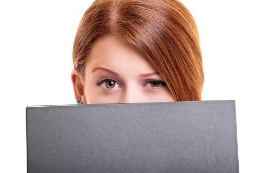 Close up portrait of a young woman hiding her face behind a book, with one brow up looking at the camera suspiciously, isolated on white background. Face expression of doubt, suspicion, distrust.