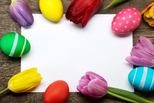 Hand-painted easter eggs with tulips on blank greeting card over wooden background copy space for text