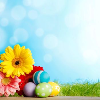 Beautiful painted easter eggs and flowers over geen meadow background