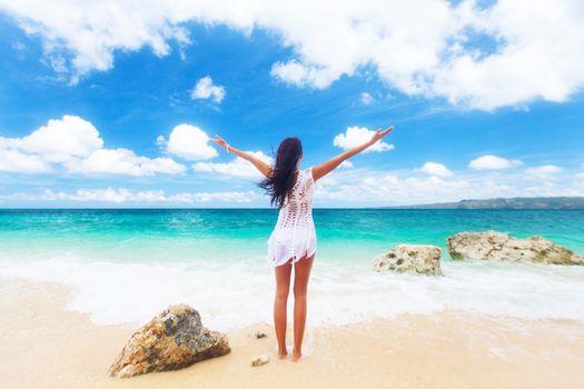 Summer freedom on the beach. Joyful woman raising arms to the sky, enjoying travel and vacation on tropical beach