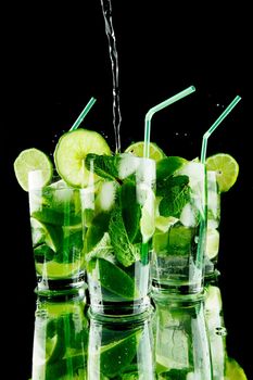 Pouring fresh mojito cocktail in glasses isolated on black background