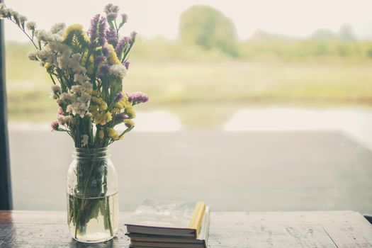 flower bouquet in glass vase and book on wooden table near window