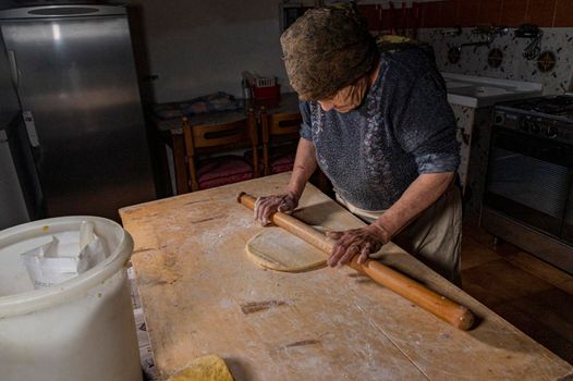 grandmother rolling out freshly kneaded dough to make tagliatelle