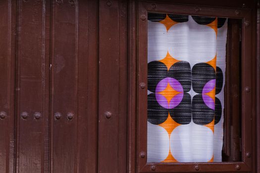 Close-up of an old wood door painted in magenta with a small window covered with a colourful curtain