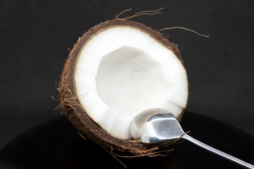 Half a coconut with pulp and a dessert spoon on a gray background.Half a coconut close up.