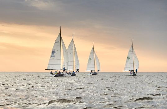 Russia, St.Petersburg, 05 September 2020: Some sailboats in a list goes by sea, the sky of pink color, the storm sky, regatta. High quality photo