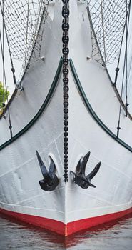 Nasal part of a sailing frigate of white color with an anchor on a nose, bright reflection in water. High quality photo